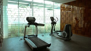 A gym with two treadmills and an elliptical machine, large windows, and a brick-patterned wall. - Big Size with City View @ 3BR Lexington Apartment (Jakarta)