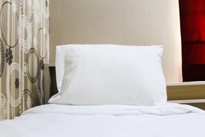 A neatly made bed with white bedding and a pillow, a headboard with a simple design, and a patterned curtain on the left. - Stylish and Convenient 2BR Green Bay Pluit Apartment (Jakarta)