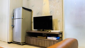 Een knus woongedeelte met een koelkast, een flatscreen televisie op een houten standaard en een klein kastje eronder.