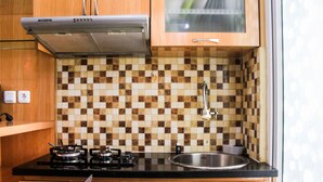 A compact kitchen with a gas stove, a sink, and a tiled backsplash. - Comfortable and Fully Furnished 1BR Green Pramuka Apartment (Jakarta)