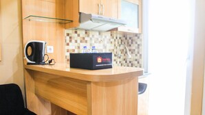 A compact kitchen with a wooden countertop, a kettle, a box labeled 'traveli', and a tiled backsplash. - Comfortable and Fully Furnished 1BR Green Pramuka Apartment (Jakarta)