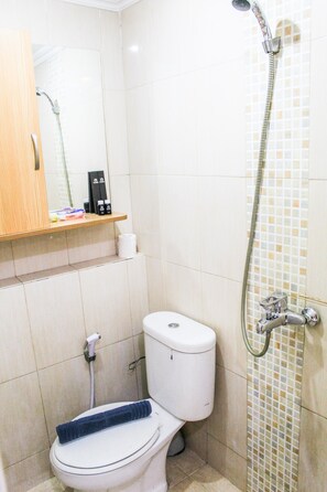 Une salle de bain équipée de toilettes, d’une douche et d’une étagère où sont rangés les articles de toilette.
