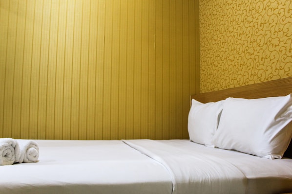 Un lit bien fait, avec du linge de lit blanc et des oreillers, une serviette enroulée et une tête de lit en bois.