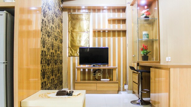 A compact living space with a flat-screen TV mounted on a wooden cabinet, a small table with a remote control, and a glass cabinet with decorative items. - Comfortable and Fully Furnished 1BR Green Pramuka Apartment (Jakarta)