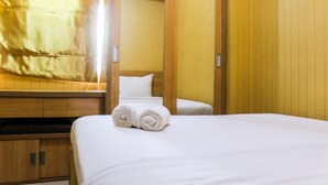 A hotel room with a bed, a wooden wardrobe, and a white pillow. - Comfortable and Fully Furnished 1BR Green Pramuka Apartment (Jakarta)