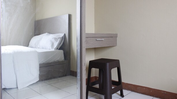 A bedroom with a bed, a nightstand, a small stool, and a wall-mounted cabinet. - Minimalist 3BR Gateway Cicadas Ahmad Yani Apartment (Bandung)