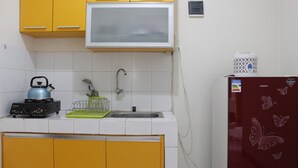 A compact kitchen with yellow cabinets, a microwave, a kettle, and a refrigerator with butterfly decals. - Minimalist 3BR Gateway Cicadas Ahmad Yani Apartment (Bandung)
