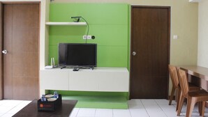 A room with a TV on a white cabinet, a small table with a tray of items, and two wooden doors. - Minimalist 3BR Gateway Cicadas Ahmad Yani Apartment (Bandung)