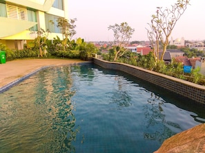 A swimming pool with clear water, surrounded by greenery and a modern building.