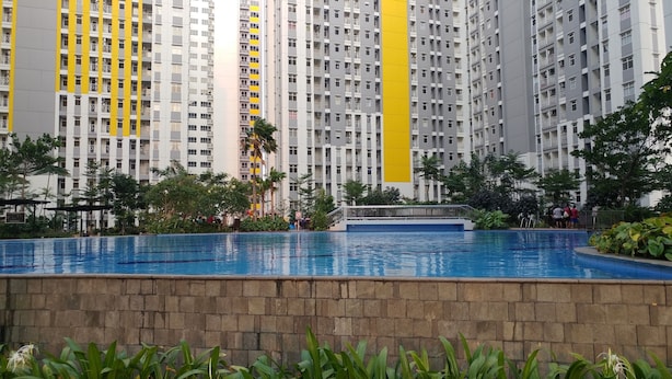 A residential building with multiple balconies, a swimming pool, and surrounding greenery. - Pool View 2BR Apartment @ Springlake Summarecon (Bekasi)