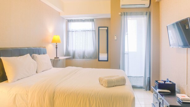 A hotel room with a large bed, a bedside lamp, a flat-screen TV, and a window with curtains. - New Furnished Studio Apartment at Gunung Putri Square (Gunung Putri)