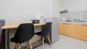 A compact kitchen with a wooden table, two black chairs, a grey refrigerator, and a coffee machine. - City View 2BR Bogorienze Apartment near The Jungle Fest (Bogor)