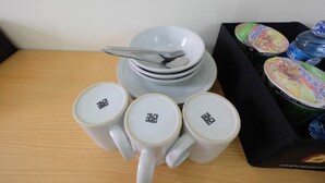 A table with stacked plates, a fork, and a tray containing a water bottle and a can of soda. - City View 2BR Bogorienze Apartment near The Jungle Fest (Bogor)