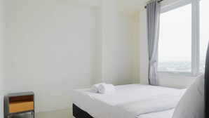 A clean, minimalist hotel room with a neatly made bed, a small bedside table, and a window with curtains. - City View 2BR Bogorienze Apartment near The Jungle Fest (Bogor)