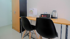 A small room with a wooden desk, two black chairs, a white coffee machine, a travelio sign, and a kettle. - Studio Apartment Bogorienze Resort near The Jungle Water Adventure (Bogor)