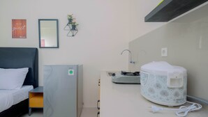 A hotel room with a bed, a small refrigerator, a microwave, a sink, and a wall-mounted shelf with a plant. - Cozy Studio Bogorienze Resort Apartment (Bogor)