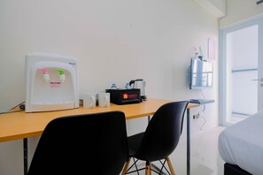 Ein Hotelzimmer mit Schreibtisch, zwei schwarzen Stühlen, Wasserspender, Kaffeemaschine und einer Minibar.