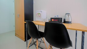 A small room with a wooden desk, two black chairs, a white coffee machine, a travelio sign, and a kettle. - Cozy Studio Bogorienze Resort Apartment (Bogor)