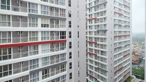 A high-rise building with multiple balconies and a red stripe running horizontally across the facade. - Comfortable Studio Apartment at Taman Melati near Universitas Indonesia (Depok)
