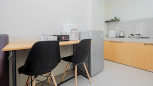 A compact kitchen with a wooden table, two black chairs, a grey refrigerator, and a coffee machine.