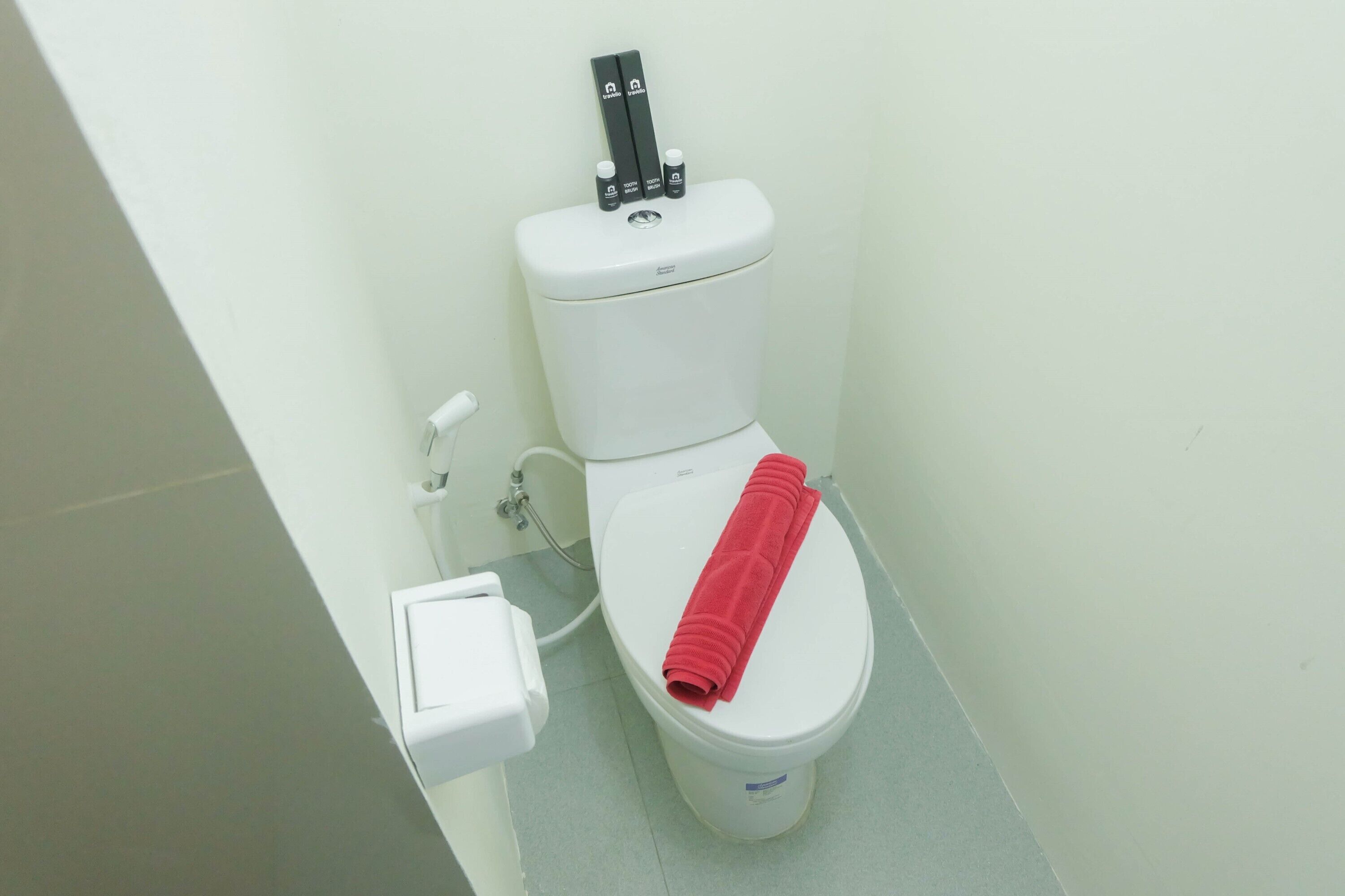 A white toilet with a red towel on the seat and a bidet attachment on top.