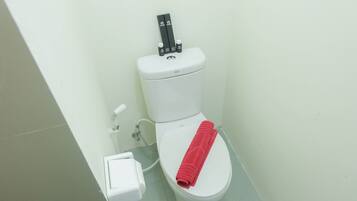 A white toilet with a red towel on the seat and a bidet attachment on top.