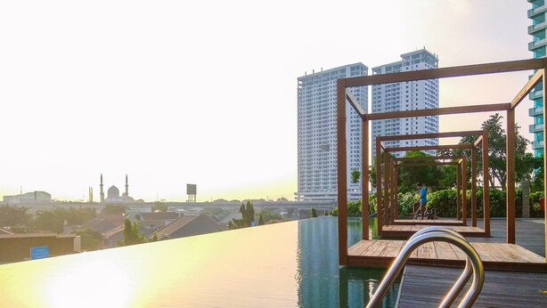 Een dakterras zwembad met een houten dek en metalen reling, met uitzicht op een stadsbeeld met wolkenkrabbers en een moskee.