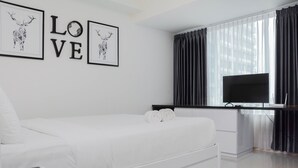 Een moderne hotelkamer met een wit bed, een bureau met een flatscreen televisie en herten kunstwerken in een lijst aan de muur.