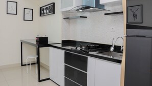 Een moderne keuken met een zwart aanrecht, witte kastjes, een roestvrijstalen spoelbak en een ingebouwde kookplaat. Er staat een klein wit krukje en er hangen afbeeldingen aan de muur.