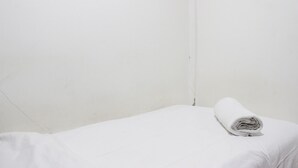 Un lit simple avec une couverture blanche soigneusement pliée, dans une pièce aux murs blancs et unis.