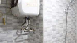 Une salle de bain avec un mur recouvert de carreaux blancs, une pomme de douche fixée au mur et un chauffe-eau.
