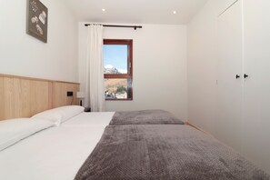 Un dormitorio con cabecera de madera, dos camas, una ventana con vista a la montaña y una puerta.