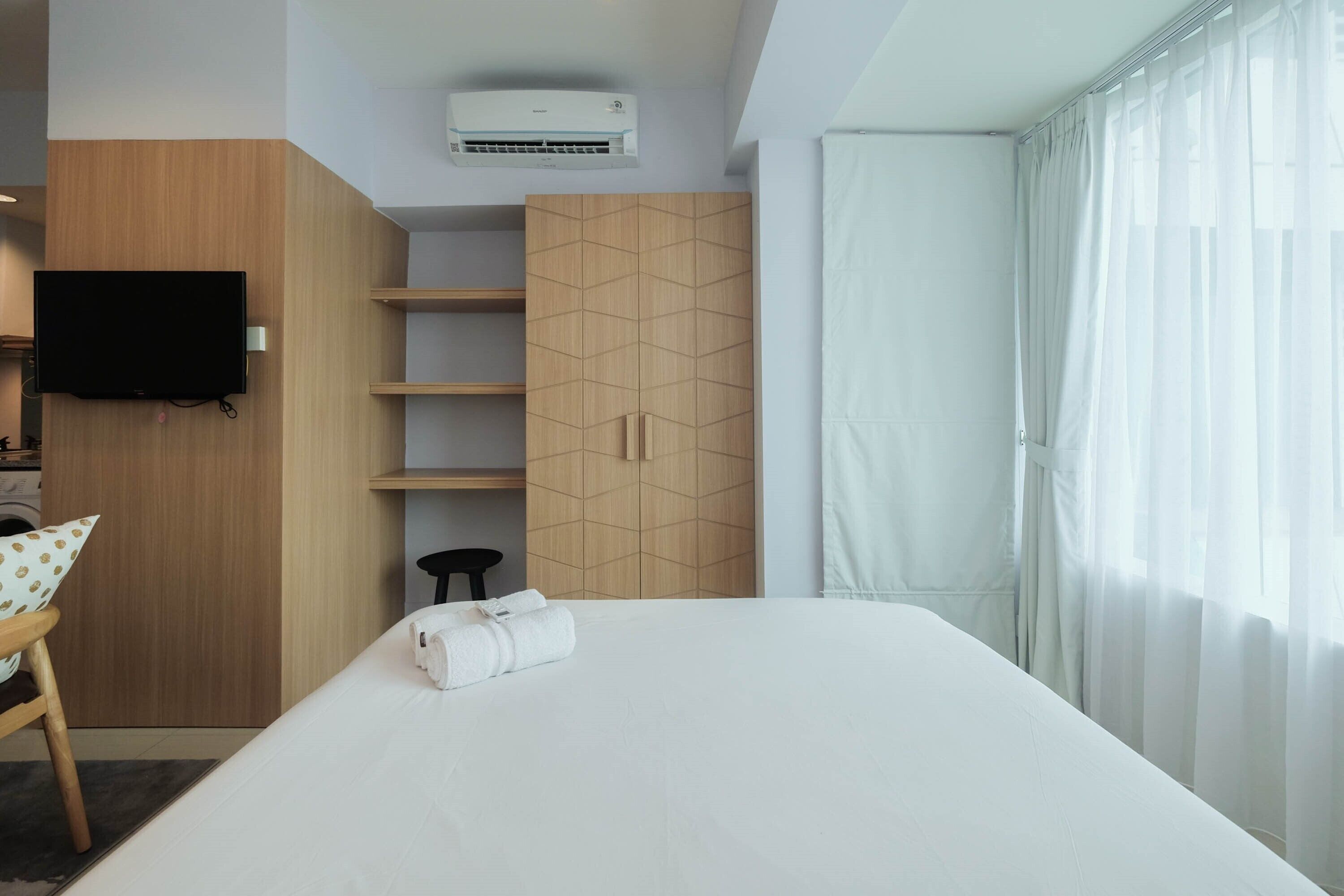 A hotel room with a bed, a TV mounted on the wall, a wardrobe, and a window with curtains.