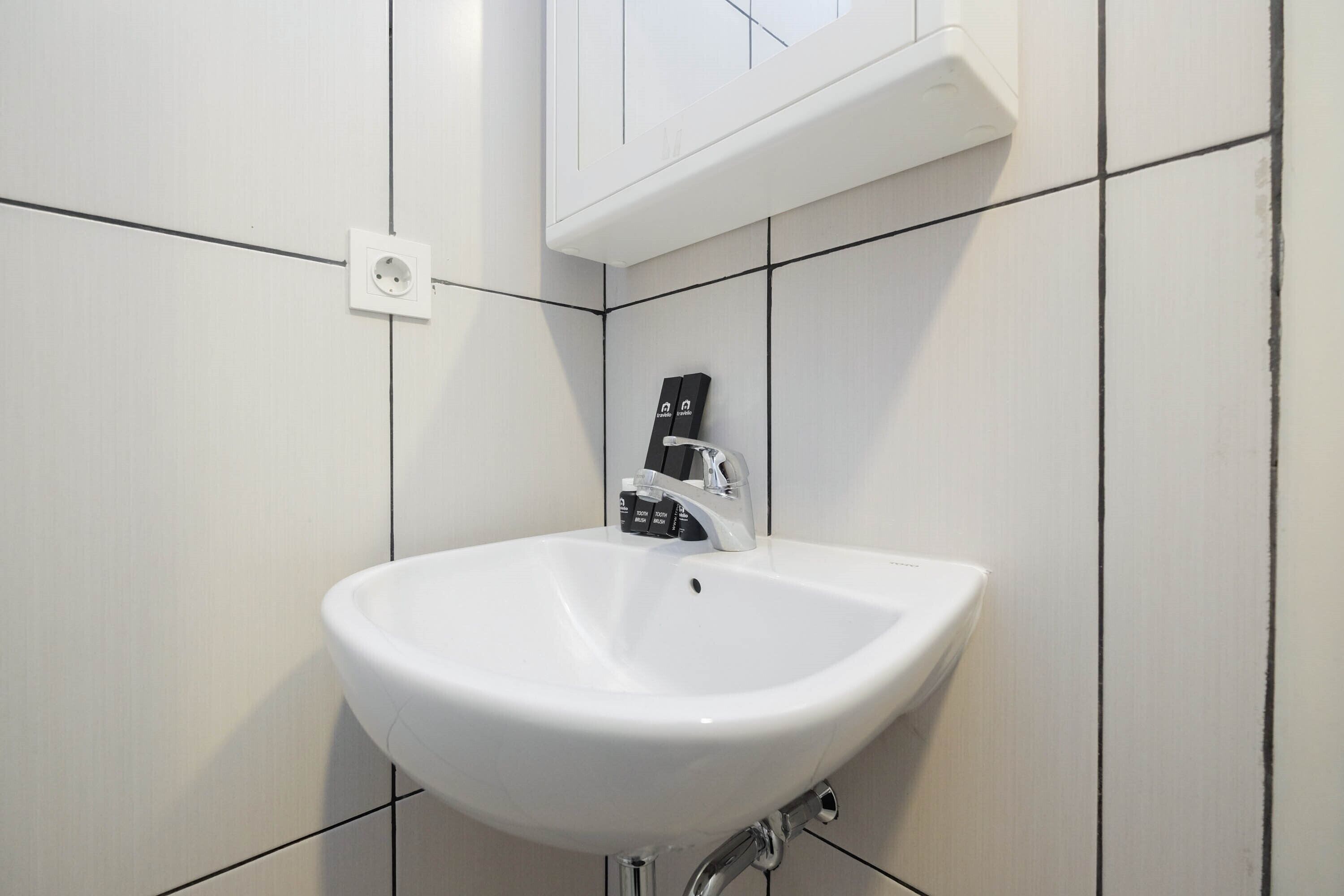 A white bathroom sink with a chrome faucet, a power outlet, and a cabinet above the sink.