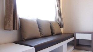 A modern, minimalist room with a built-in bench, a small white table, and a window with curtains. - Compact Studio Room @ Galeri Ciumbuleuit 2 Apartment (Bandung)