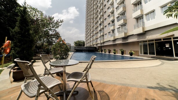 A pool area with lounge chairs and a table, surrounded by a high-rise building with balconies. - Compact Studio Room @ Galeri Ciumbuleuit 2 Apartment (Bandung)