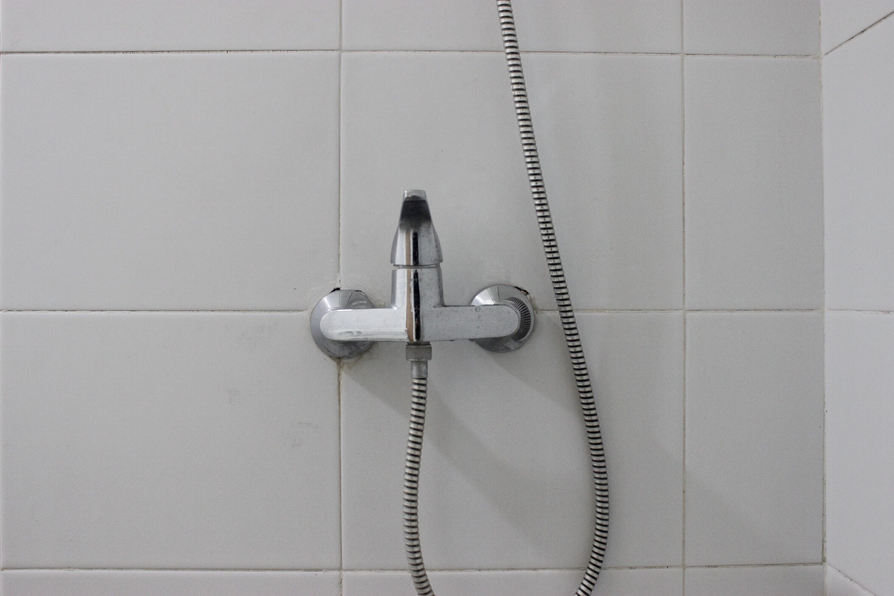 Een douche met een chromen kraan en douchekop, bevestigd aan een betegelde muur.