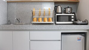 A kitchen with a microwave, toaster, and a dish rack with orange items. - Comfy & Artsy Studio at Beverly Dago Apartment (Bandung)