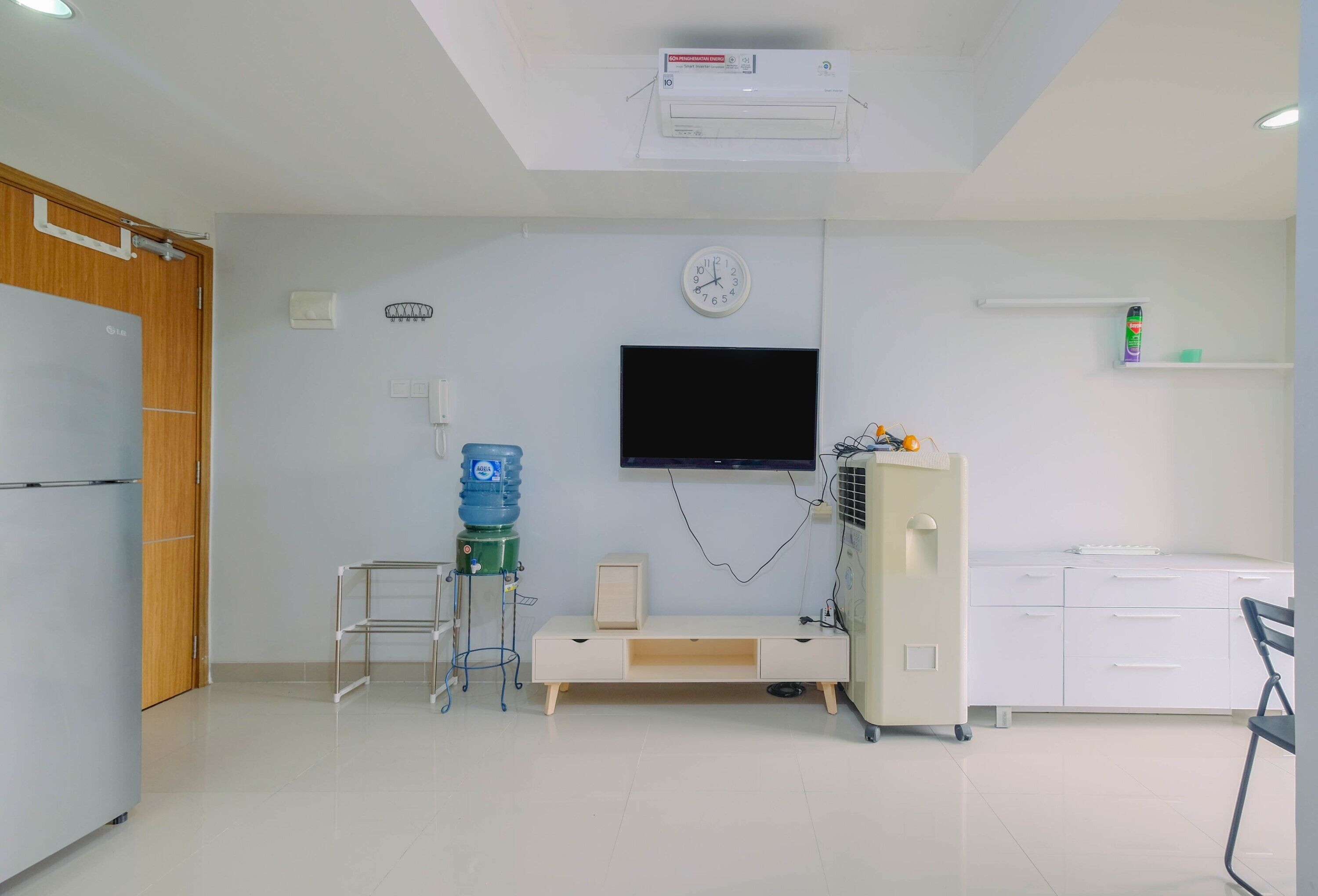 Una habitación limpia y moderna con televisión de pantalla plana, dispensador de agua, un mueble pequeño y una silla.