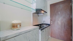 A kitchen with a marble countertop, a built-in stove, a glass shelf, and a wooden door. - Cozy and Minimalist Studio Apartment @ Mustika Golf Residence (Cikarang)