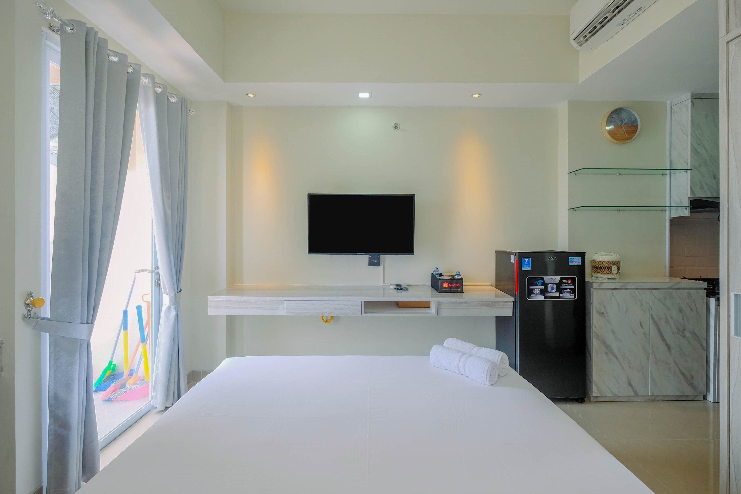 A hotel room with a bed, a flat-screen TV, a minibar, and a kitchen area.