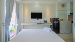 A hotel room with a bed, a flat-screen TV, a minibar, and a kitchen area. - Cozy and Minimalist Studio Apartment @ Mustika Golf Residence (Cikarang)