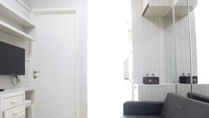 Una stanza con una televisione su un mobile bianco, un divano grigio e una porta con stipite bianco.