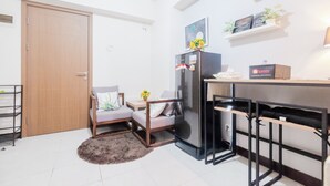 A compact kitchen with a refrigerator, a wooden door, a small dining table, and a shelf with decorative items. - Spacious and Comfortable 2BR Cinere Resort Apartment (Depok)