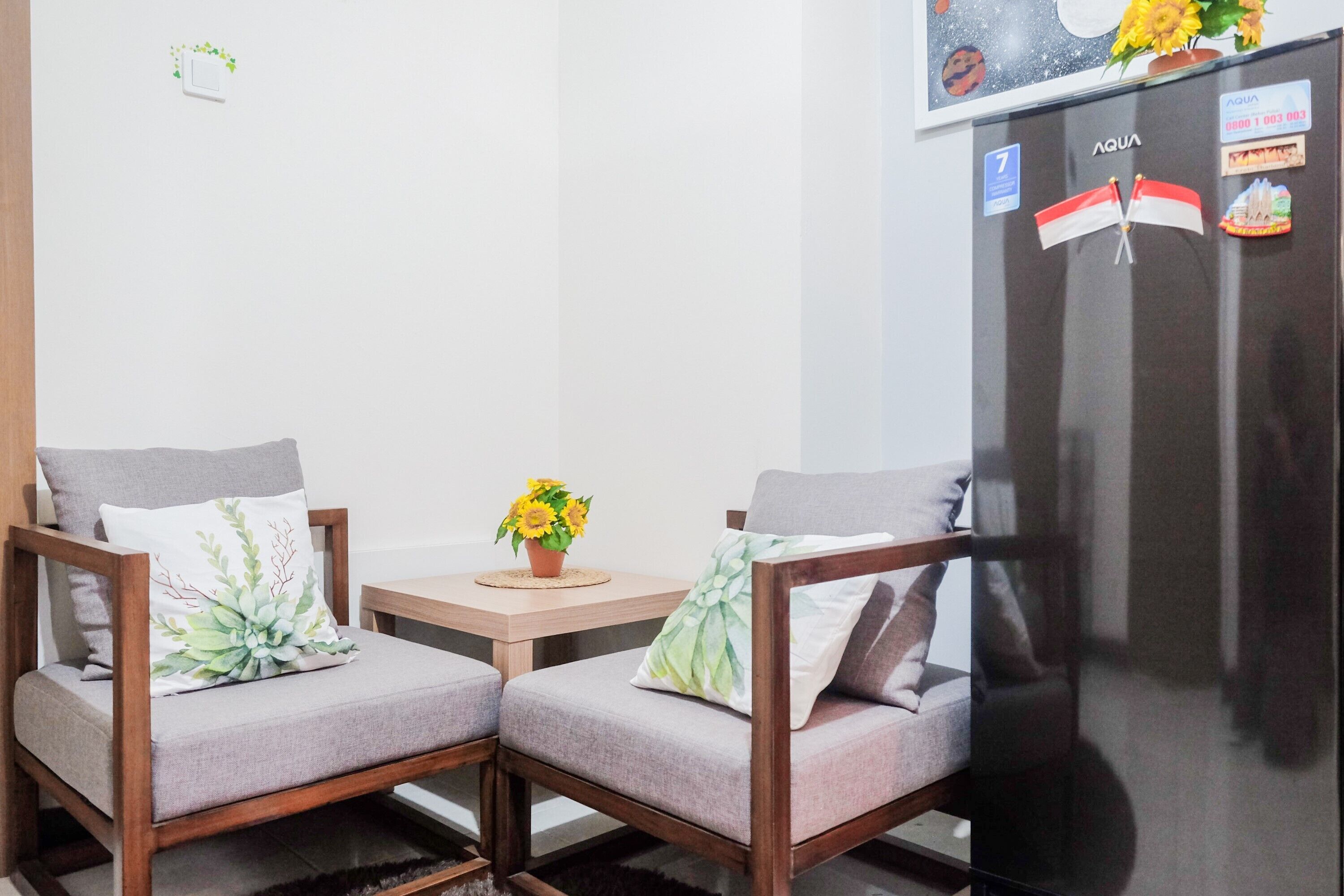 A small kitchenette with a refrigerator, two chairs, a small table, and a potted plant.