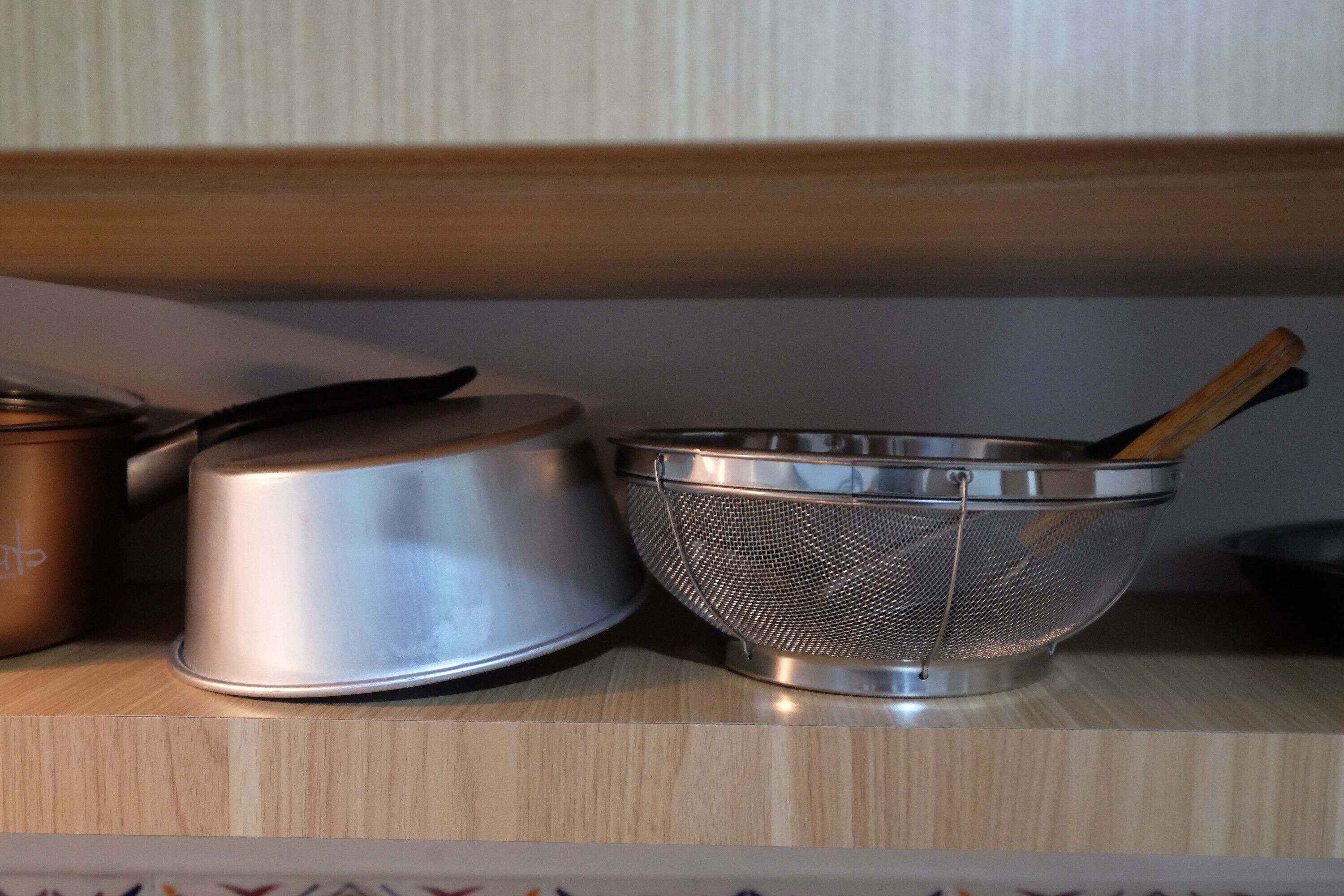 Una encimera de cocina con una olla de acero inoxidable, un colador y una cuchara de madera.