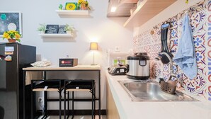 A compact kitchen with a countertop, sink, and a stove. There are two stools, a lamp, and decorative items on the shelves. - Spacious and Comfortable 2BR Cinere Resort Apartment (Depok)