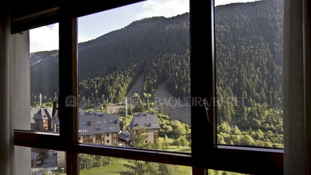 Vista a través de una ventana que muestra un paisaje montañoso con un edificio en primer plano.