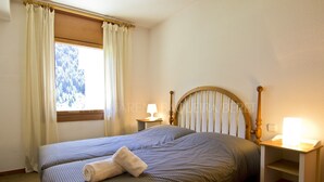 Un dormitorio con una cama, dos mesitas de noche con lámparas, un ventanal con cortinas y un cabecero de madera.