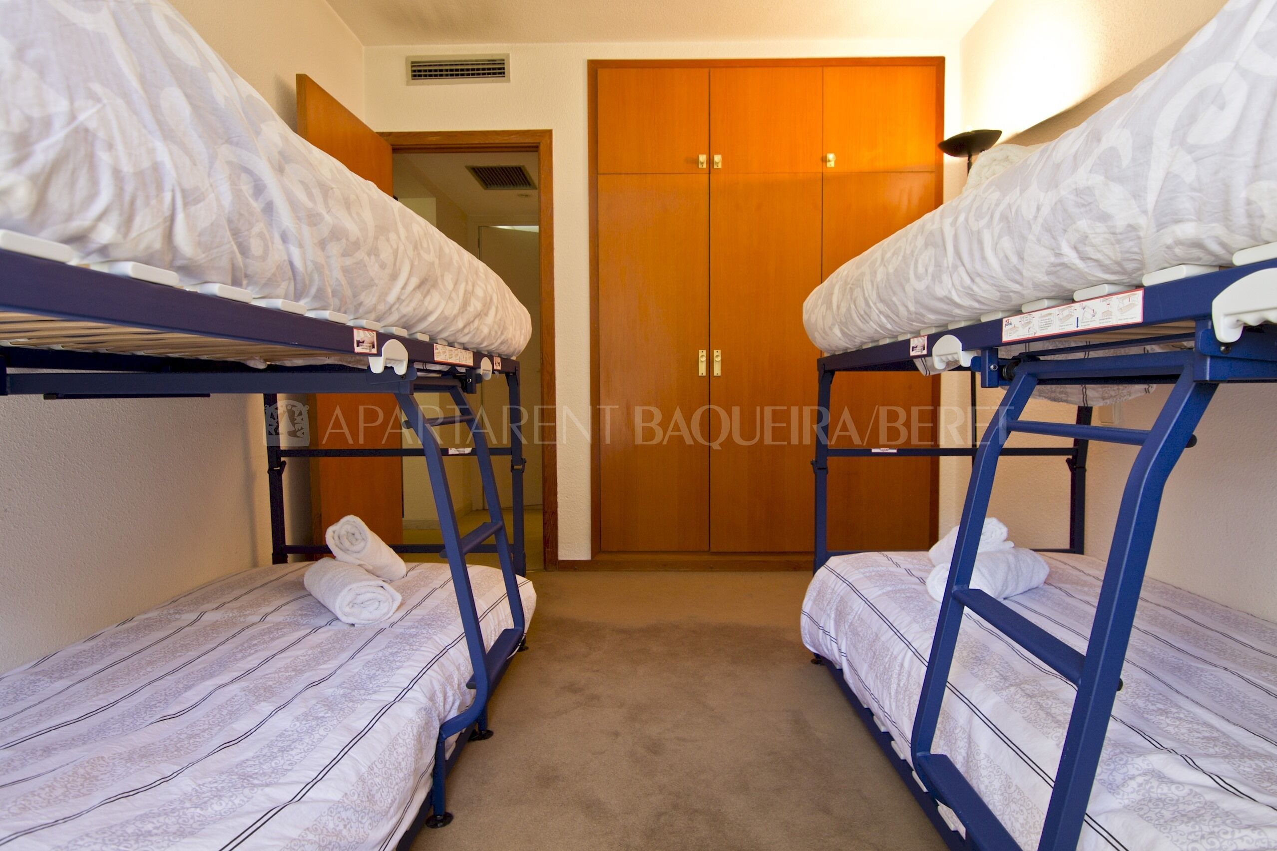 Een kamer met twee stapelbedden, een houten garderobe en een deur.